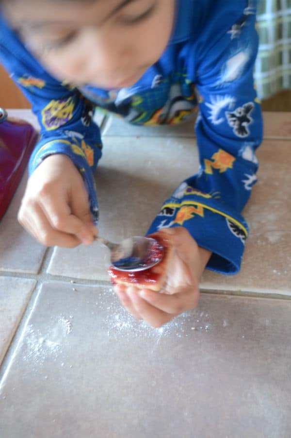 Kid decorating and filling up cinnamon cookies with jam.