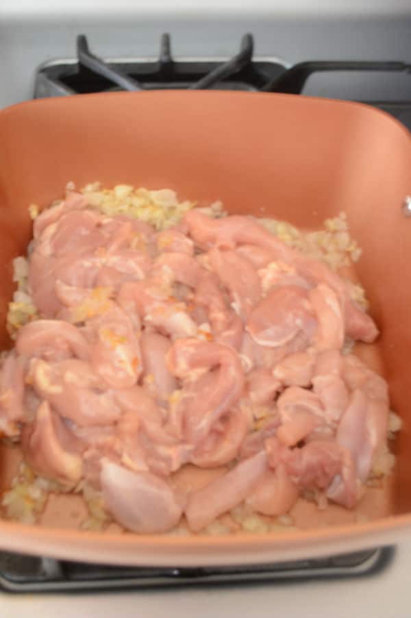 A pan of food on a stove, with Chicken and onions