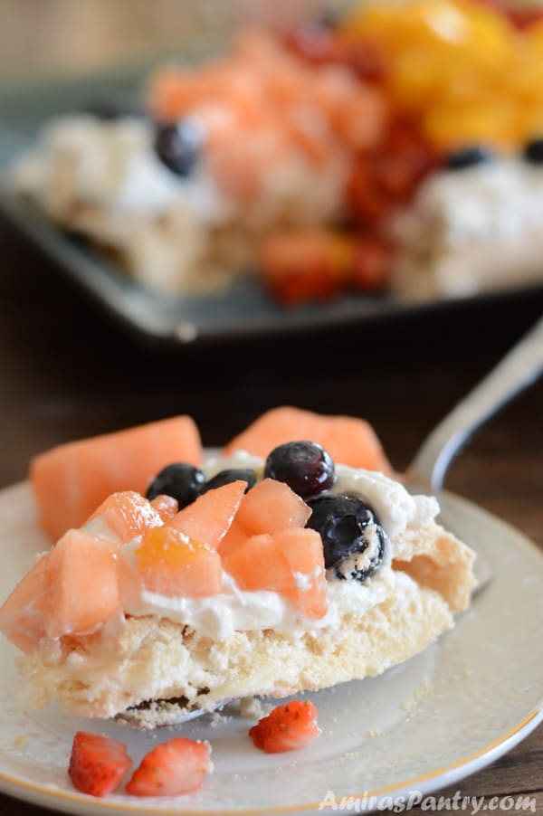 A close up of a piece of cake on a plate, with Pavlova and fruits