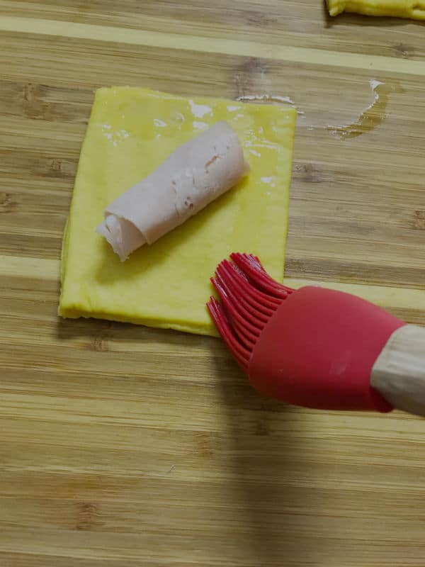 A knife sitting on top of a wooden cutting board, with meat and dough