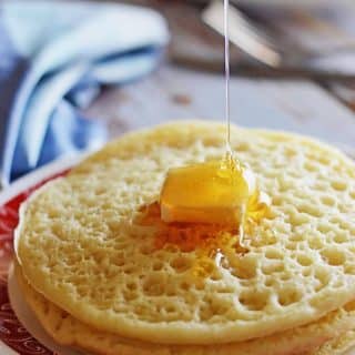 A stack of Moroccan pancakes with a square of butter on top and drizzling honey over.