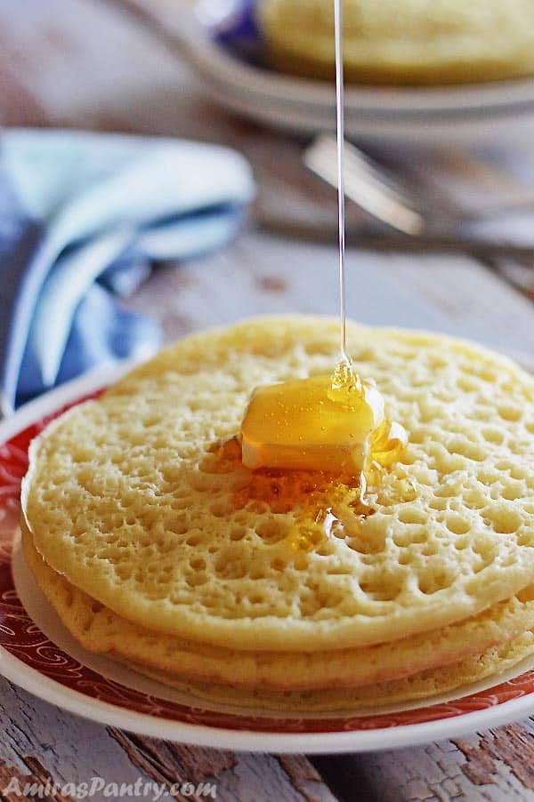 A stack of Moroccan pancakes with a square of butter on top and drizzling honey over.