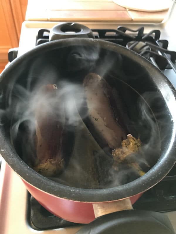 A close up of a metal pan on a stove, with water and Eggplant