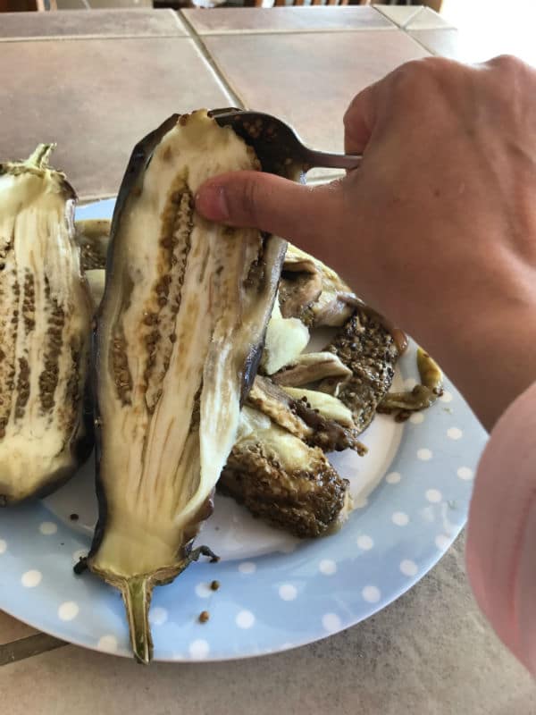 A close up of opened eggplant and hand with spoon