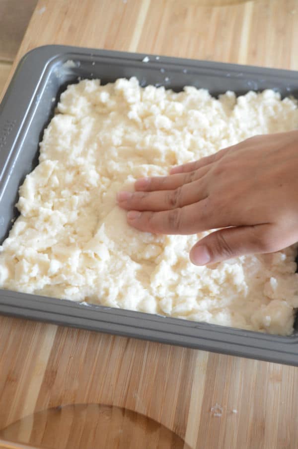 A hand mixing dough in a pan