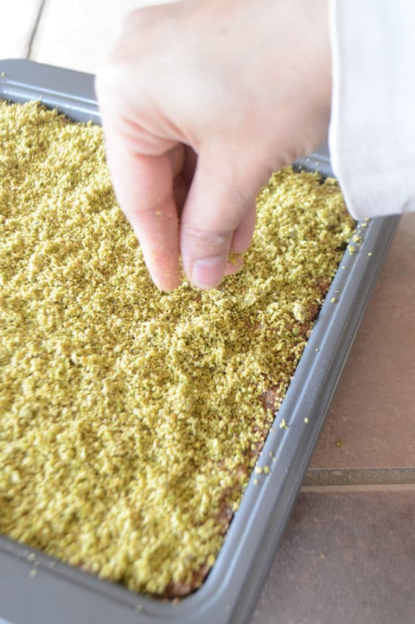 A hand mixing dough in a pan with Pistachios