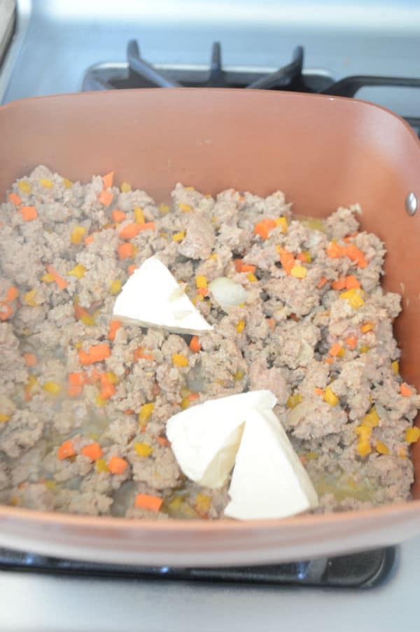 A bowl with food on a stove, with meat and vegetables