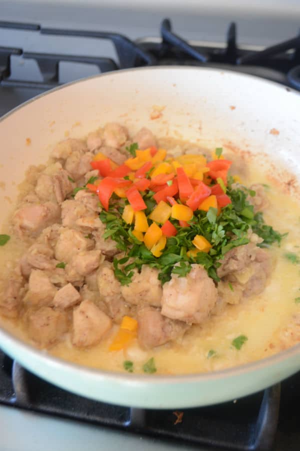 Adding bell peppers with parsley to chicken in the skillet to make the filling.