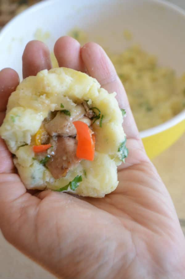 Hand holding mashed potato stuffed with chicken mixture ready to be formed into a ball.