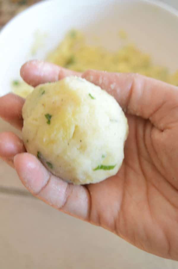 Hand holding a ball of mashed potato stuffed with chicken to make cheesy potato chicken casserole.