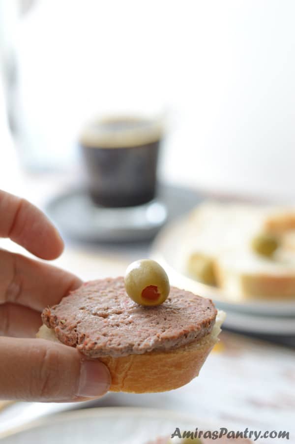 A close up of hand holding corned beef sandwich with green olive