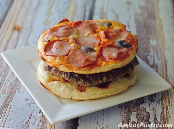 A white plate with a whole pixxa burger on it showing peperoni , cheese and olives on top.