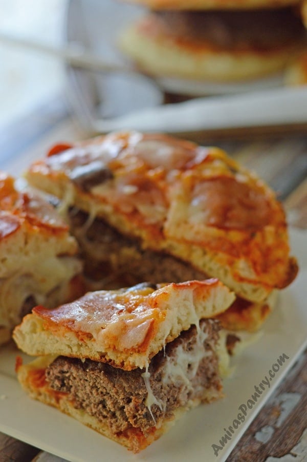 A white plate with pizza burger on it cut in half.