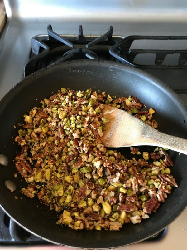 A bowl of food sitting on a pan on a stove, with nuts