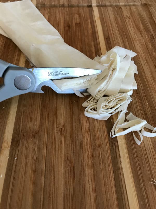 A scissor cutting strips of pastry on top of a wooden table