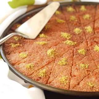 Basbousa pan, cut into diamond shapes and garnished with crushed pistachios. With a serving spatual on top.