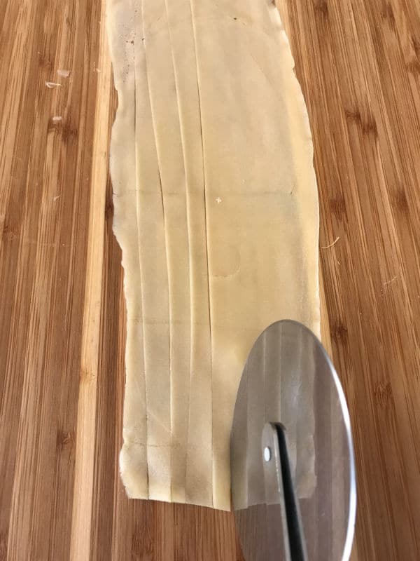 A photo showing cutting strips of dough on a wooden table