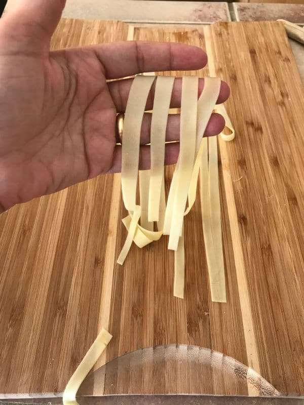 A hand holding cutting strips of dough on a wooden table
