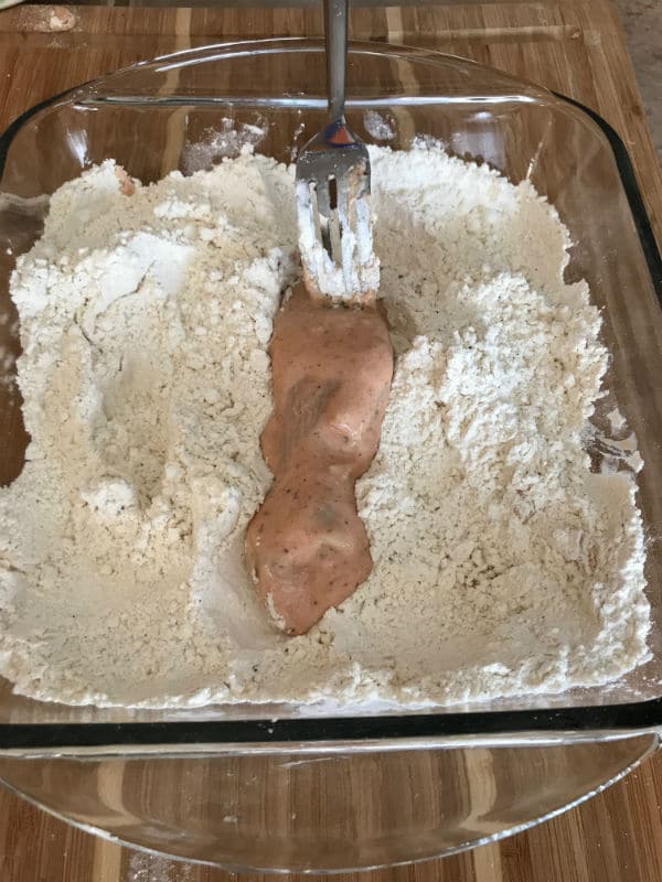 A chicken in a mixture in a glass bowl over wooden table