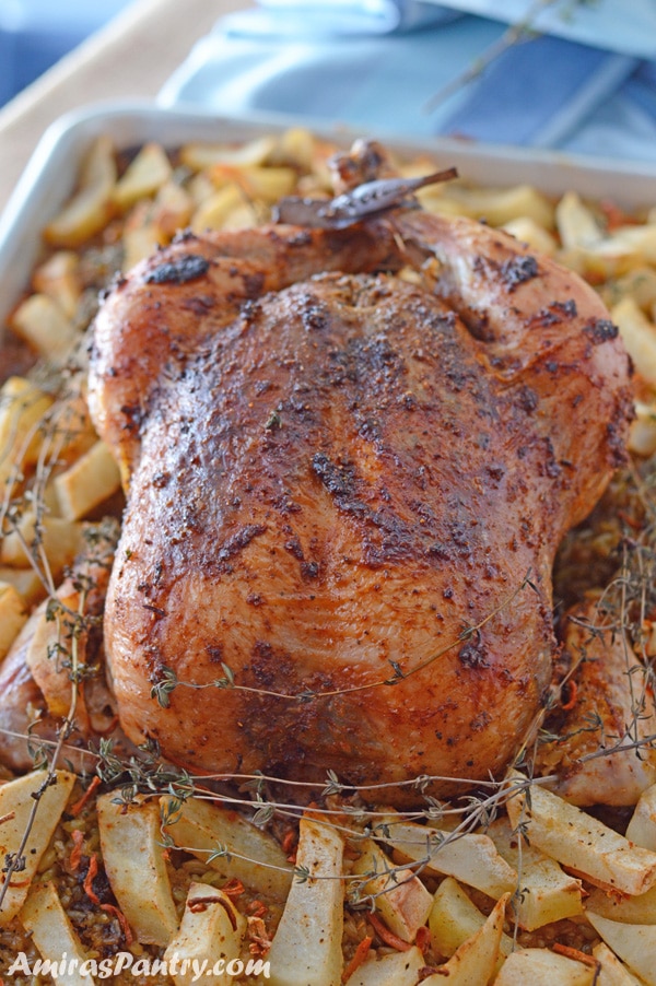 Whole chicken on a baking dish with roasted potatoes and freekeh.