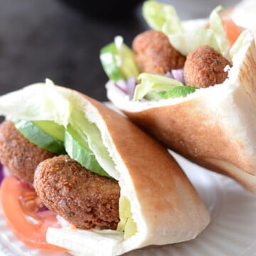 A close up of a pita bread cut on a plate, with Falafel and vegetables