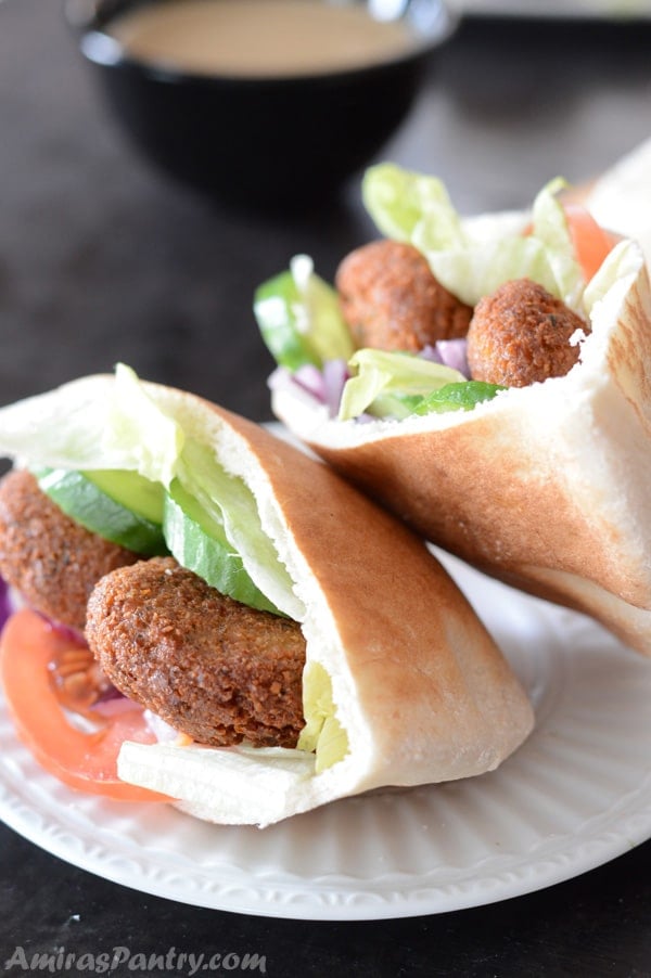 A close up of a pita bread cut on a plate, with Falafel and vegetables