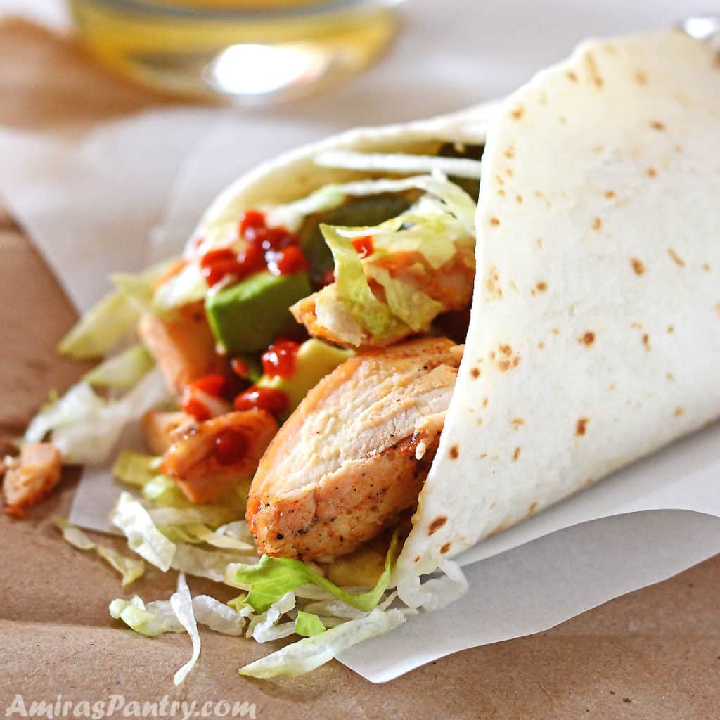 Baked Chicken Thighs wrapped in a tortilla bread with lettuce on a white parchment paper.