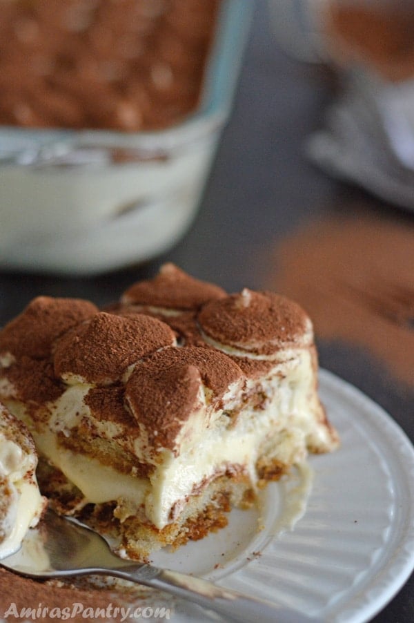 A serving of the tiramisu on a plate with a cut up small piece in a fork next to it.