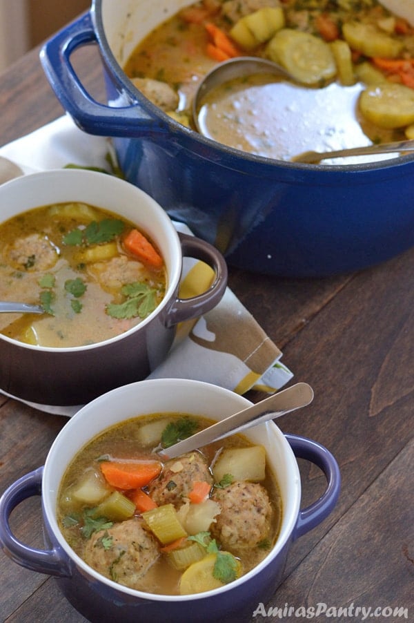 Big blue pot of Albondigas soup along with two bowl with the soup in them.