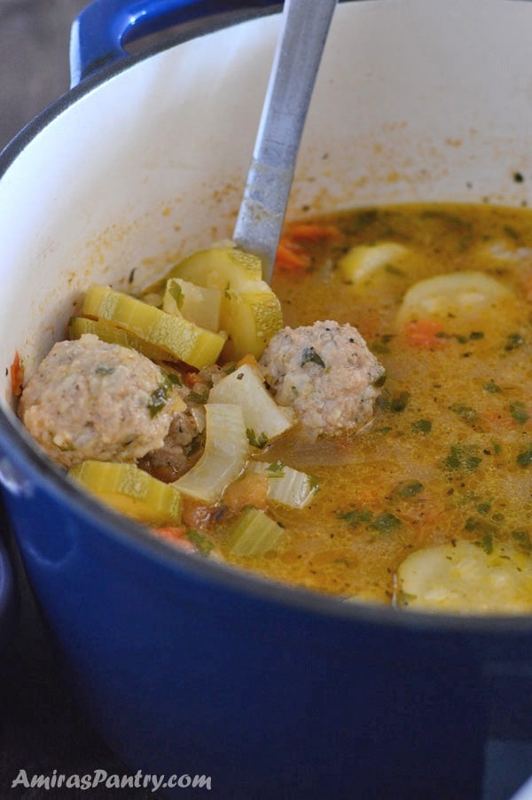 Big blue pot of Albondigas soup with a ladle in it showing the vegetables and meatballs in the soup.