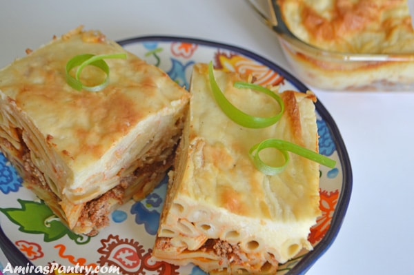 Two square pieces of baked bechamel pasta on a plate with the whole pan in the background