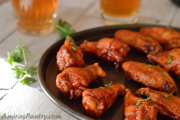 Honey BBQ Chicken wings on a big oven try with a couple of juice glasses in the background.