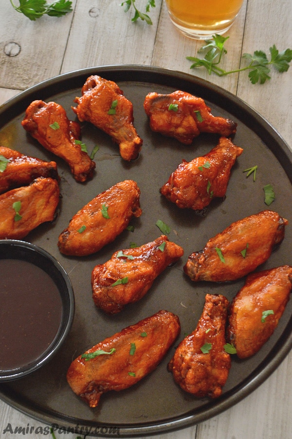 Honey BBQ chicken Wings on the baking tray with a small bowl of dipping sauce and a glass of juice on the side.