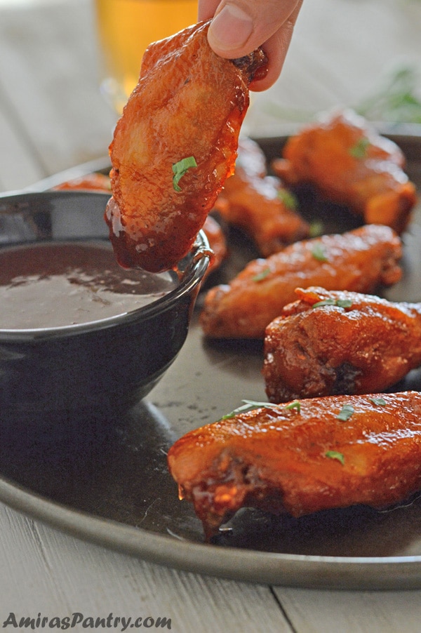 A hand holding one wing and dipping it in the dipping sauce.