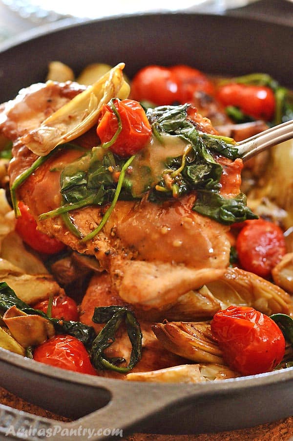 Chicken and artichokes skillet with a spoon taking a serving out.