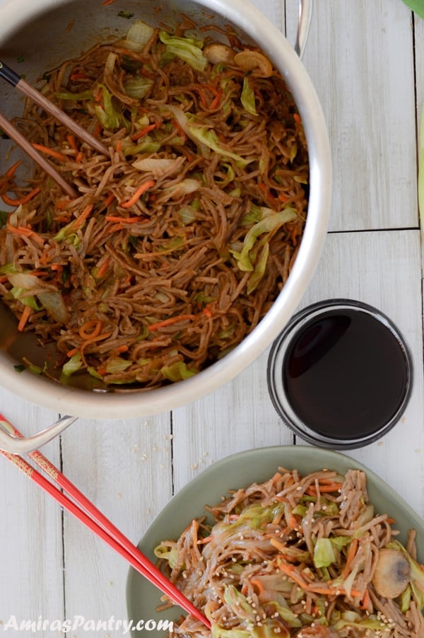 A big pot of yakisoba with sauce on the side and a plate with some yakisoba.