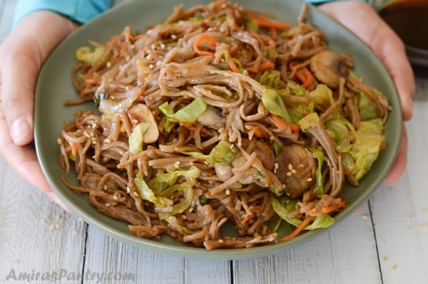 Hands holding a plate of yakisoba.