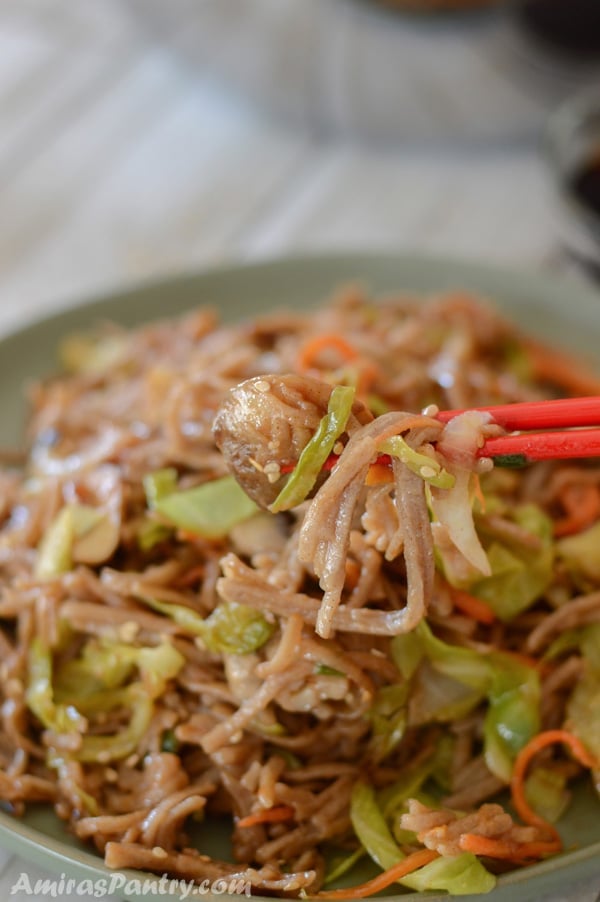 Chopsticks holding some yakisoba noodles and veggies.