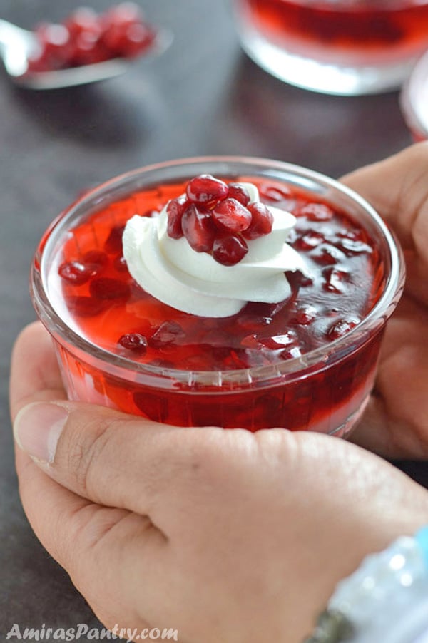 A hand holding a glass cup filled with pomegranate parfaits