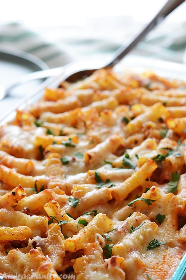 A whole pyrex of baked ziti with melted cheese on top and sprinkled with some chopped parsley.