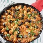 A pan with Tater tots, cheese and olives