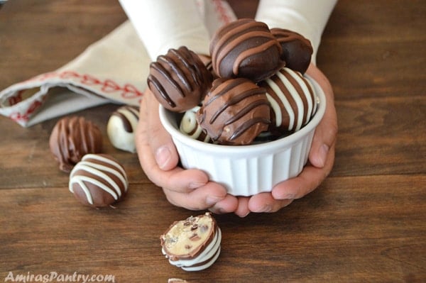 Hands holding a small bowl of chocolate chip cookie dough truffles