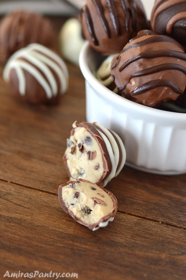 One chocolate chip cookie dough truffle cut in half on a table with bowl of stacked truffles on the side.