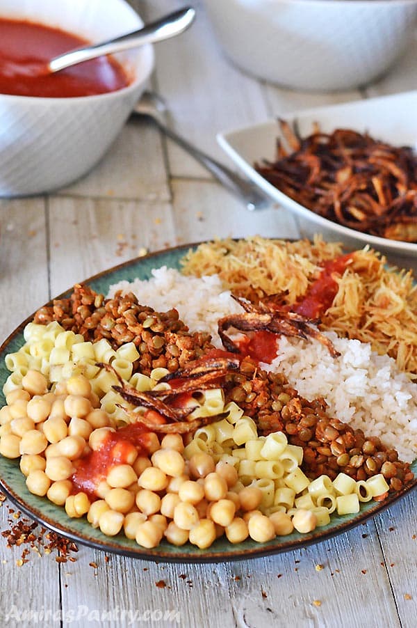 A big platter of Egyptian Koshari with vinegar tomato sauce and crunchy onion in the back