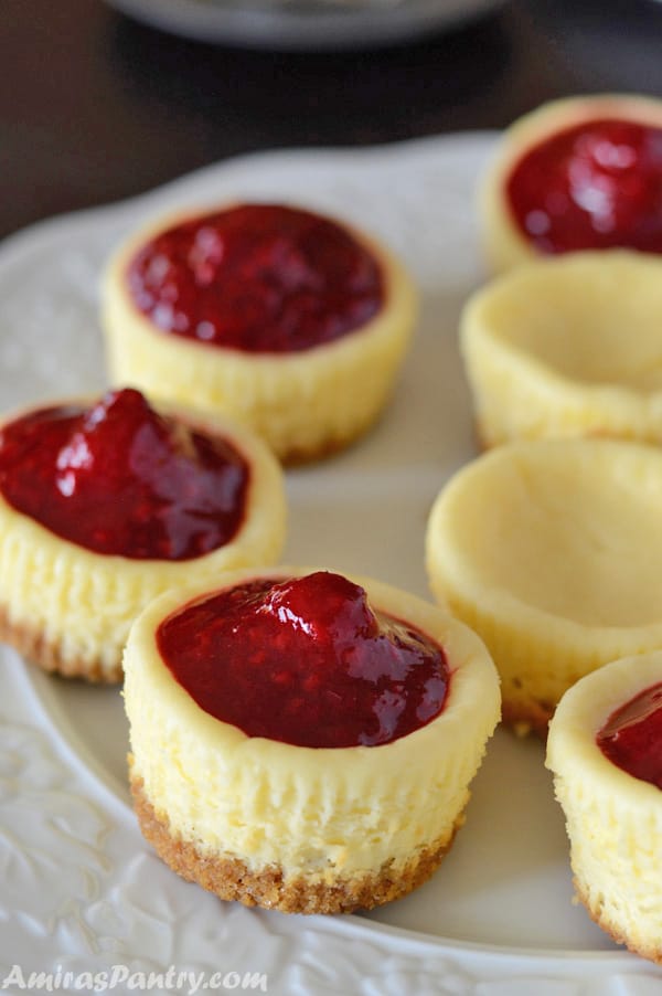 A big platter with mini raspberry cheese cakes on it, some filled with raspberries and some are plain.
