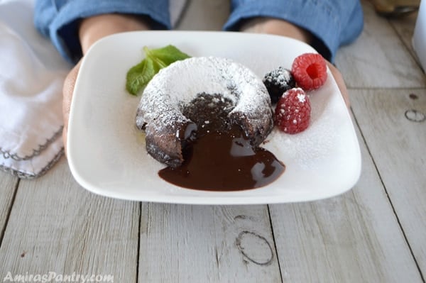 Hands serving a plate with one chocolate molten lava cake dusted with powdered sugars and berries on the side.