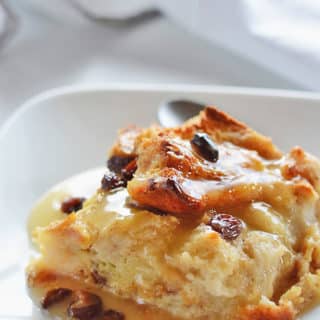 A piece of classic bread pudding on a white plate with raisins on top.
