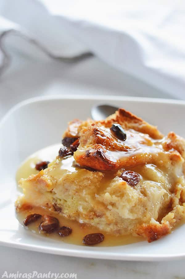 A piece of classic bread pudding on a white plate with raisins on top.