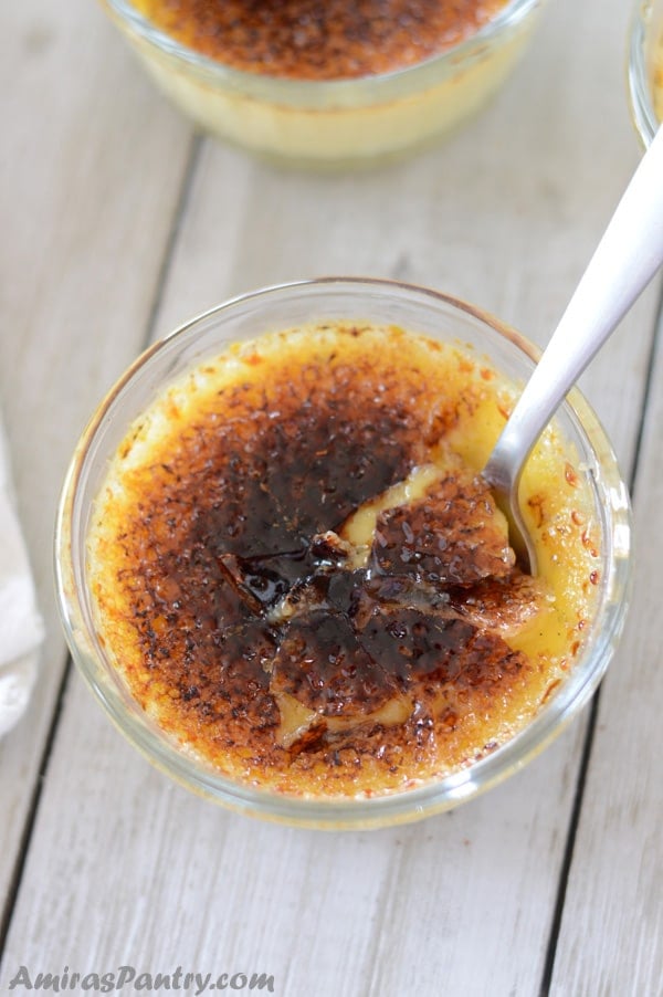 A small ramekin of easy creme brulee with a spoon in the middle and a cracked caramelized sugar layer on top.
