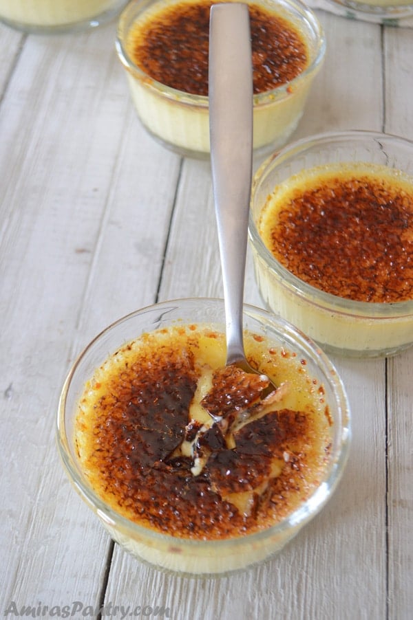 A small ramekin of easy creme brulee with a spoon in the middle and a cracked caramelized sugar layer on top with some ramekins on the back